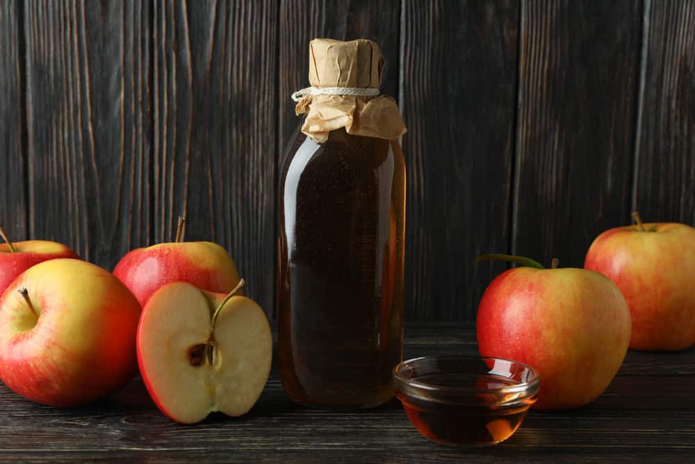 Homemade apple vinegar and ingredients on wooden background