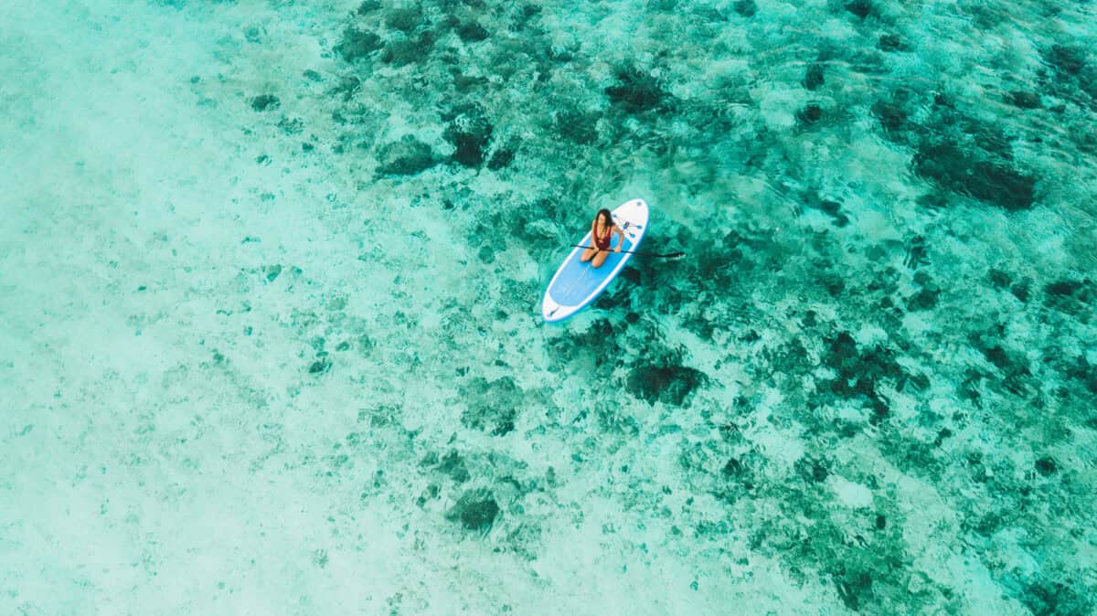 Woman sitting on sup board and enjoying turquoise transparent