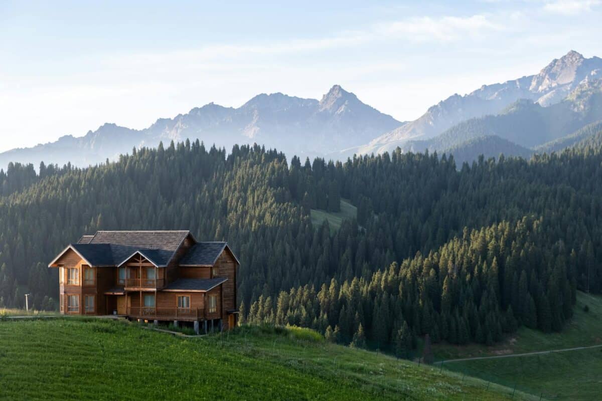 A scenic view of a wooden cabin with a mountainous backdrop in Xinjiang, China.