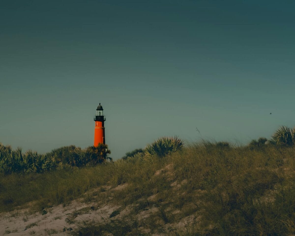 A striking orange lighthouse stands among the dunes under a darkening sky.