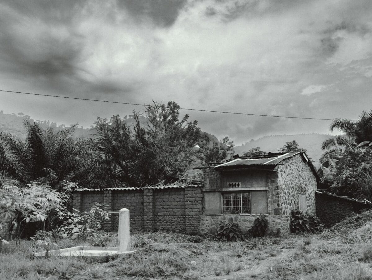 A rustic stone house surrounded by lush greenery in rural Bujumbura under an overcast sky.