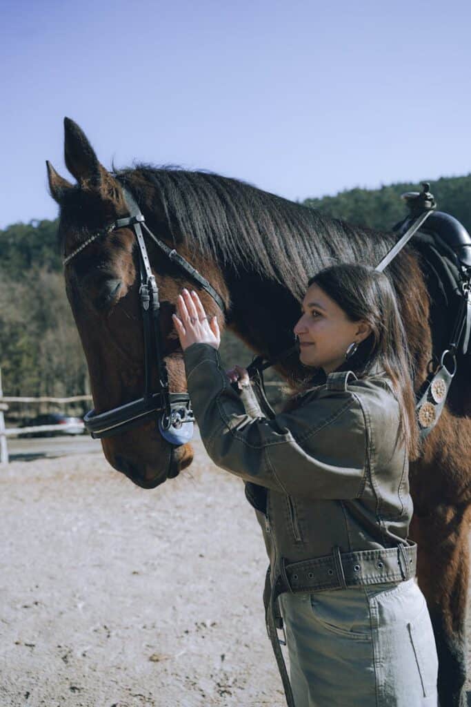 A woman gently strokes her horse outdoors under a clear blue sky, enjoying a peaceful moment together.
