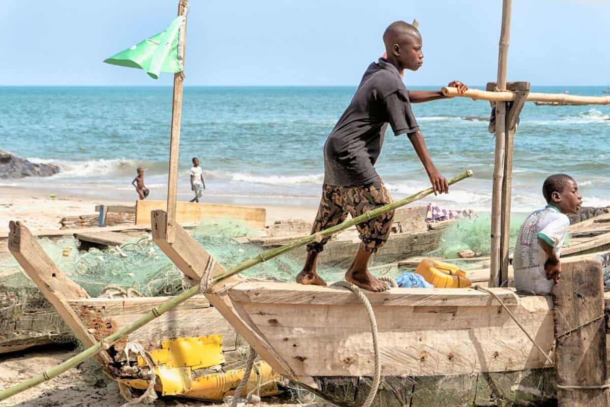Children navigating a traditional wooden fishing boat on the coast of Elmina, Ghana.
