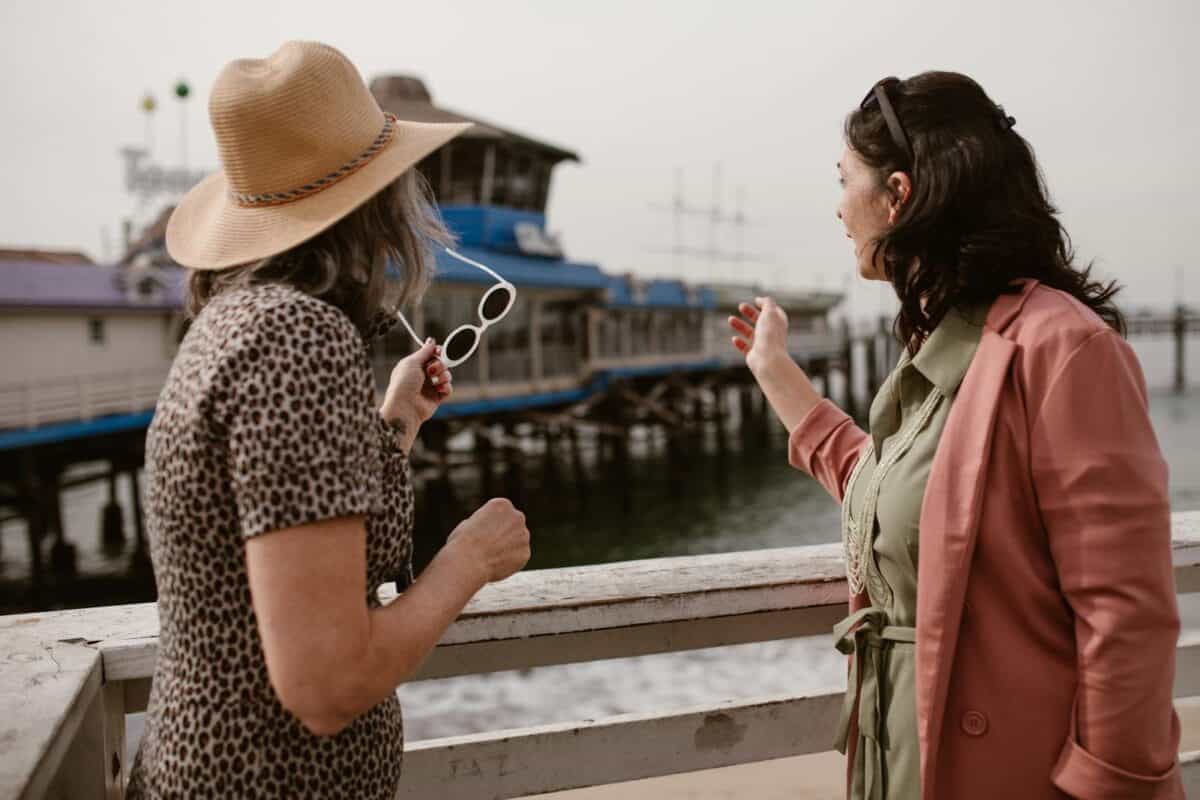 Two women at a pier, enjoying a day by the sea, sharing a moment.