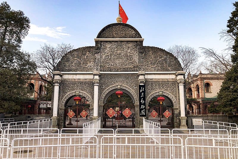 Ornate entrance gate of the Beijing Zoo, featuring intricate stone carvings, traditional Chinese lanterns, and a Chinese flag on top.