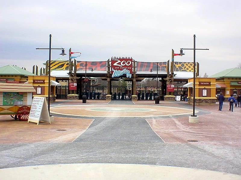 Entrance of Columbus Zoo and Aquarium featuring a bold sign, animal-patterned banners, and a ticket booth on a cloudy day