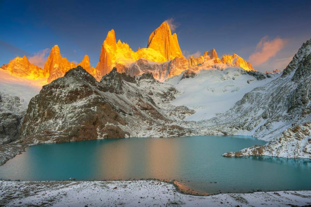 A stunning winter landscape featuring glowing mountains and a serene lake at sunrise.