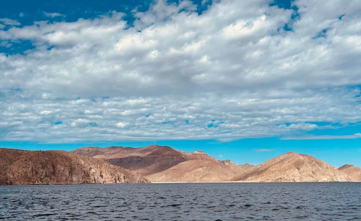 Peaceful view of mountains under a bright blue sky with fluffy clouds.