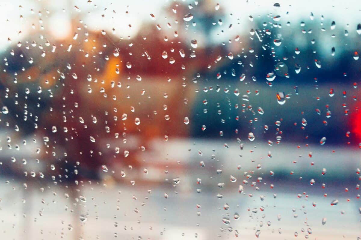 Rain droplets on window creating a blurry, colorful bokeh effect with a moody ambiance.