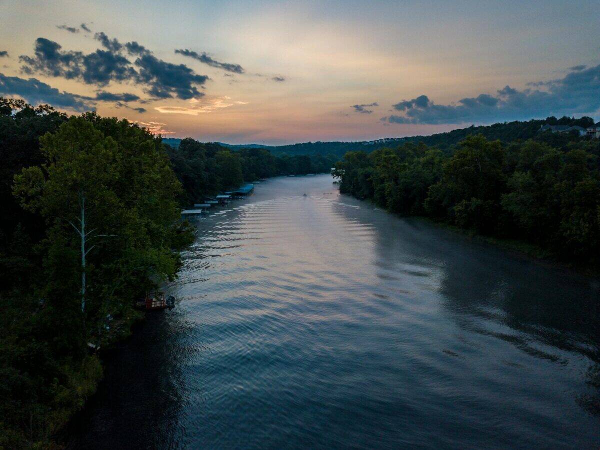 Aerial view of a serene river with lush trees at sunrise, capturing nature's tranquility in Hollister, Missouri.