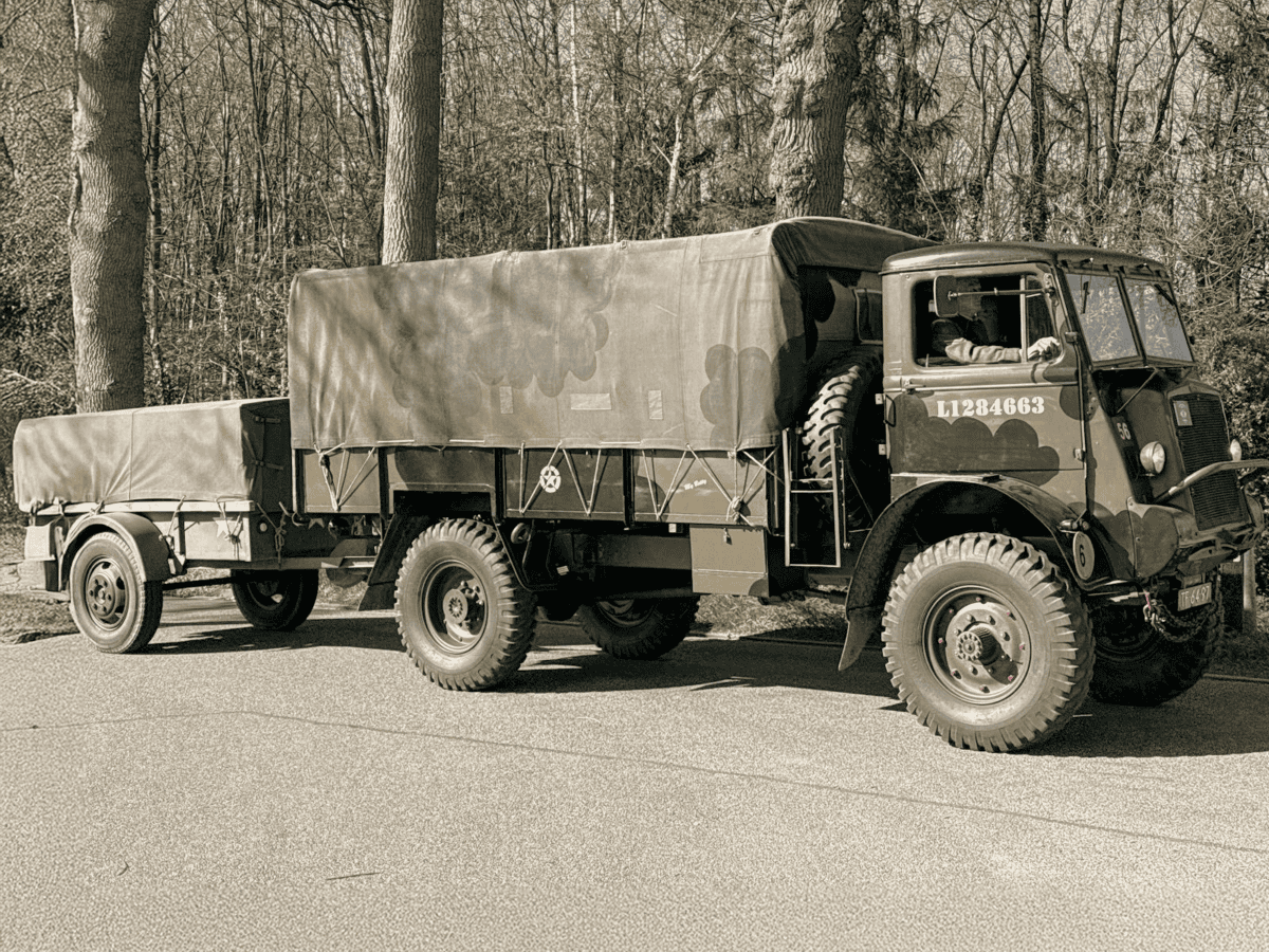 Classic military truck with trailer parked on a forest road during the day.