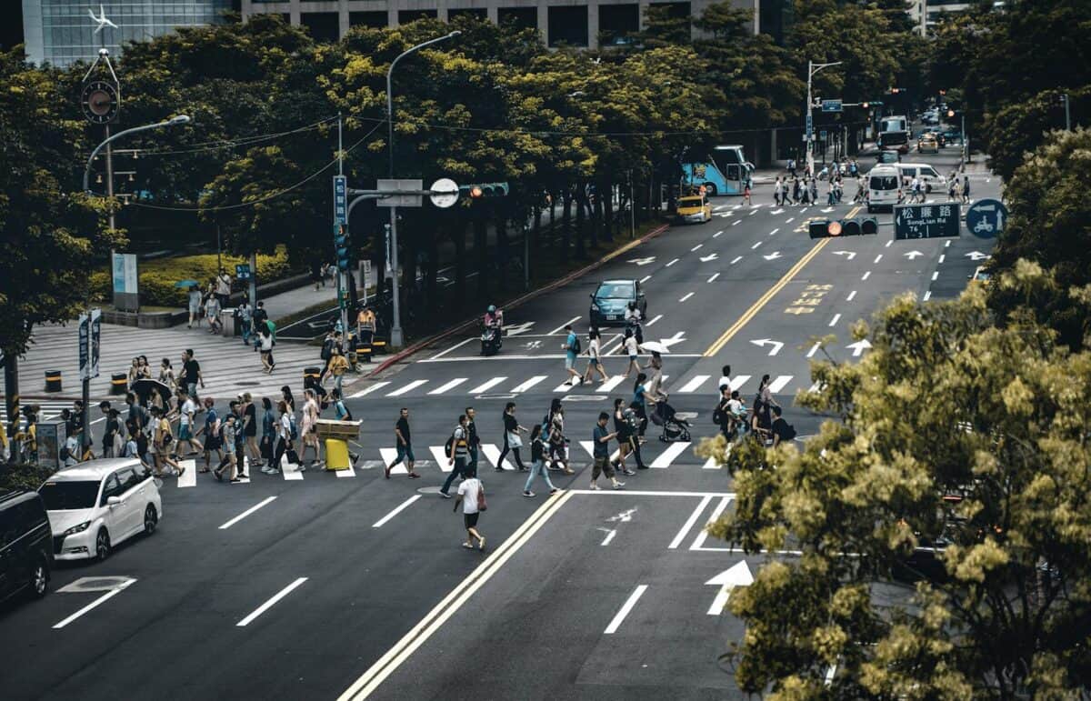 Crowded crosswalk in city with diverse pedestrians and vehicles at intersection.