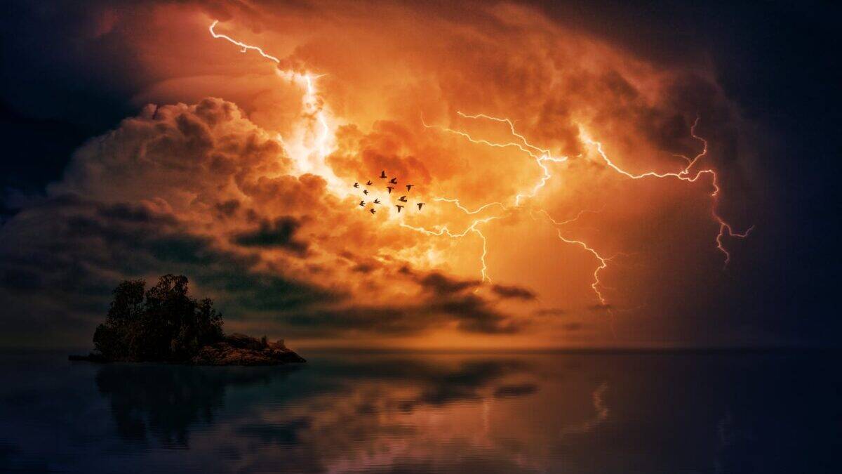 Flock of birds fly during a dramatic lightning storm over a tranquil ocean islet.