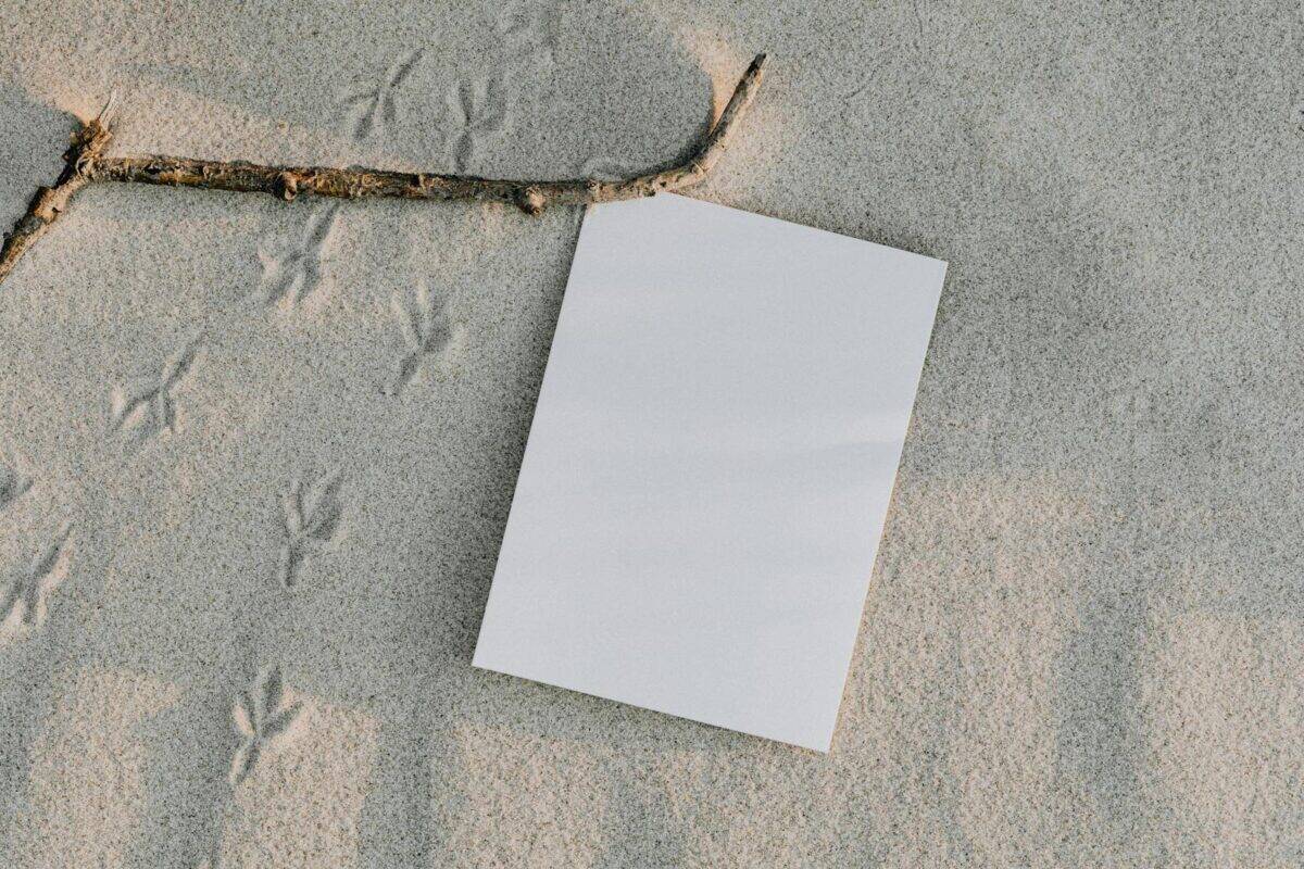 A blank sheet of paper on sand featuring bird tracks and a branch, perfect for mockups.