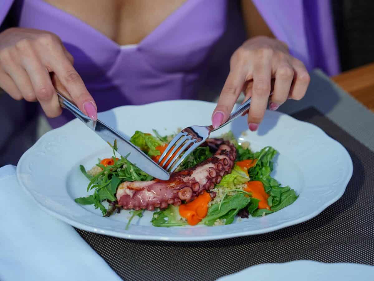 Woman enjoying an octopus salad with fresh greens outdoors. Vibrant and appetizing.