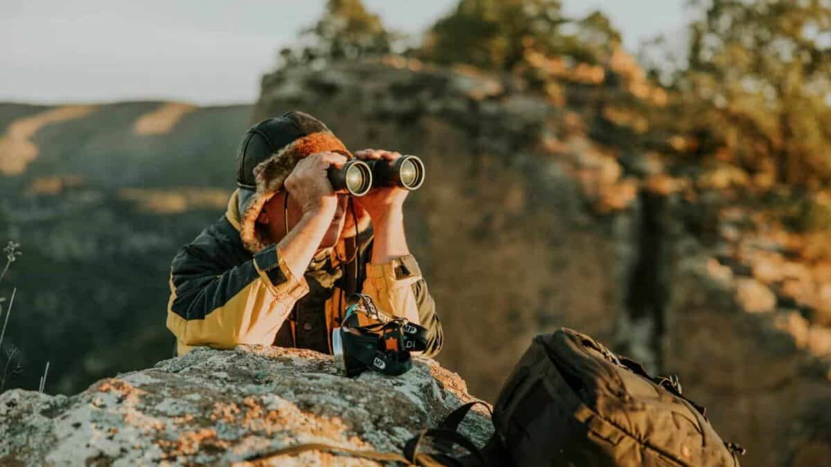 An adventurer observes through binoculars in a picturesque canyon landscape during dusk.