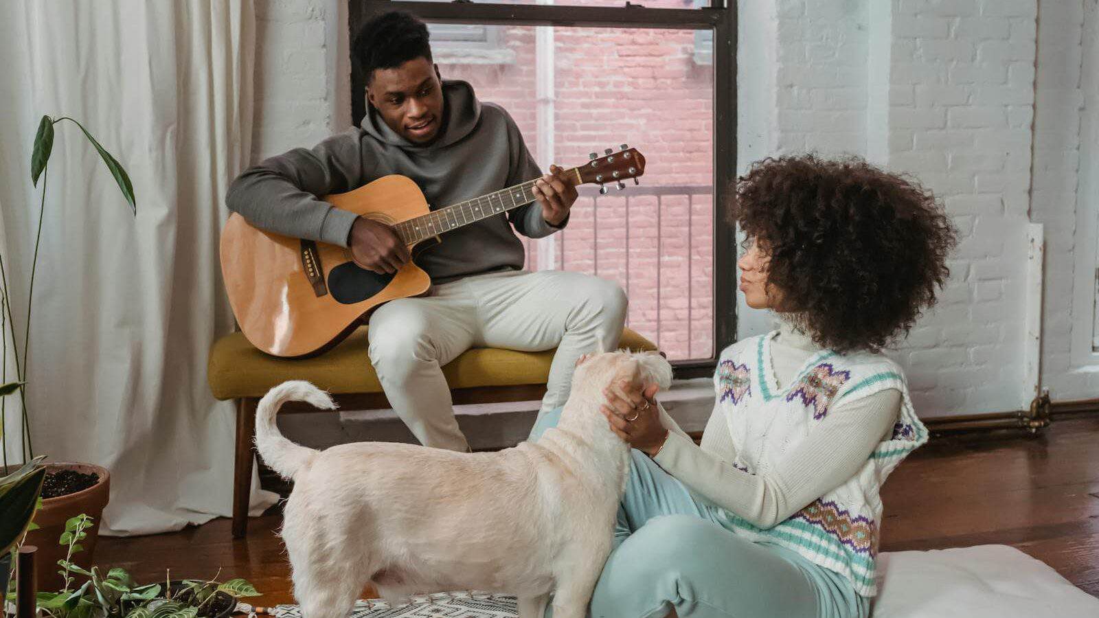 A couple enjoys music at home, with a guitar and their dog. A scene of warmth and connection.