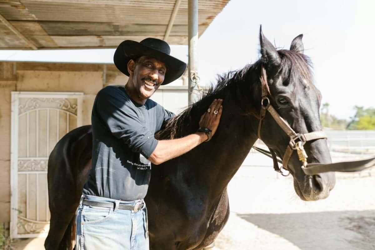 Smiling cowboy petting his horse on a sunny ranch day, showcasing rural lifestyle and companionship.
