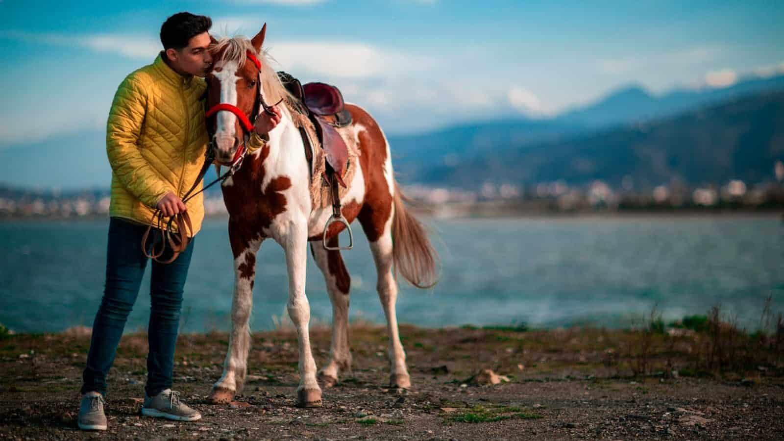 woman in brown jacket and blue denim jeans standing beside brown and white horse during daytime