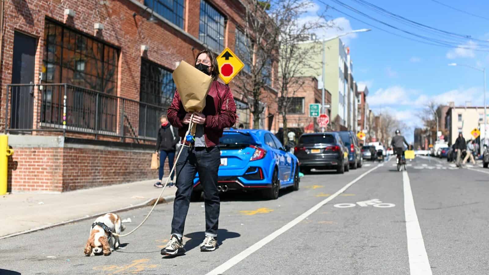 man in yellow jacket and black pants standing beside blue car during daytime