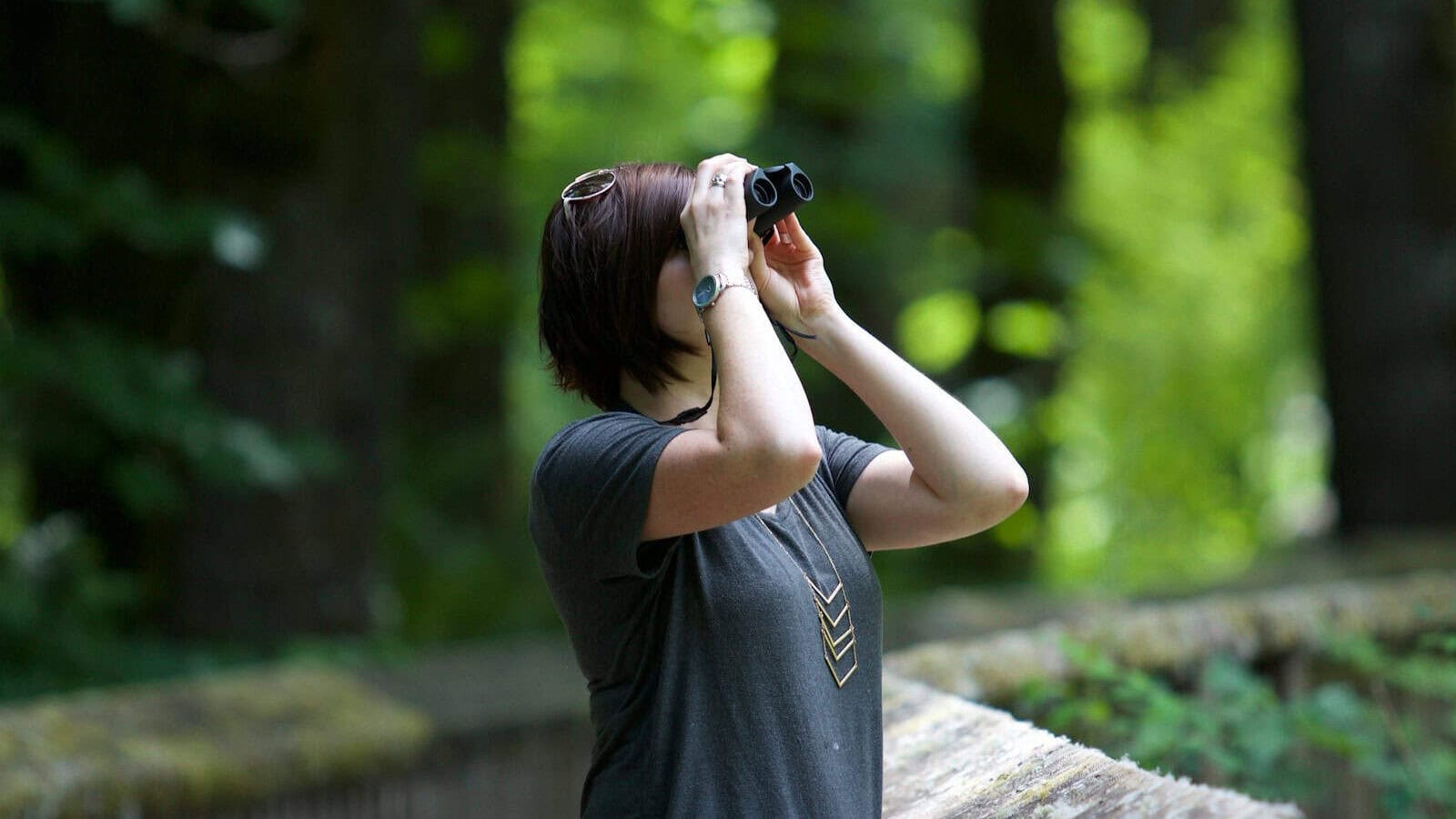 selective photography of woman holding binoculars looking upward outdoors