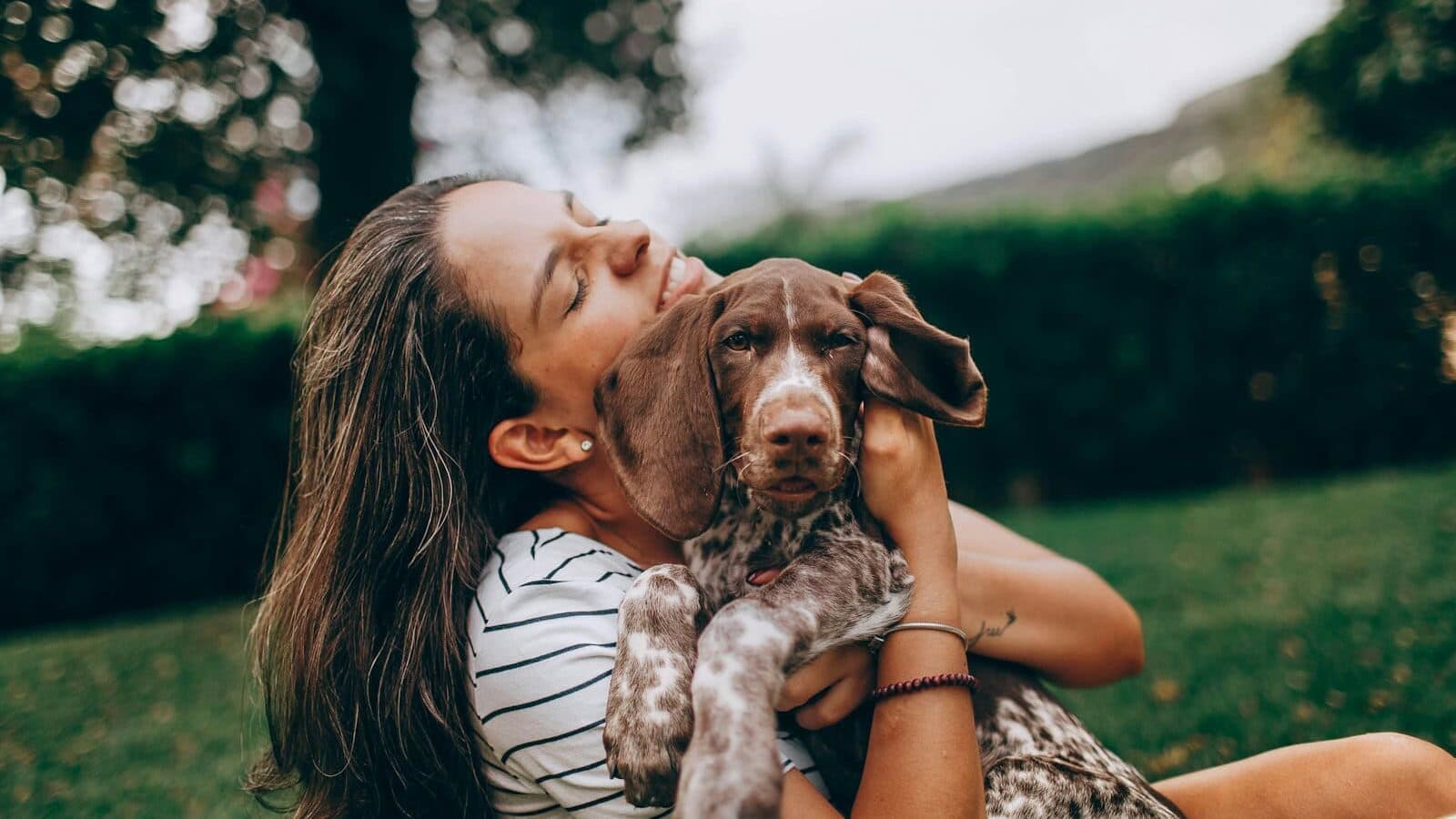 woman in white and black stripe tank top hugging brown and white short coated dog