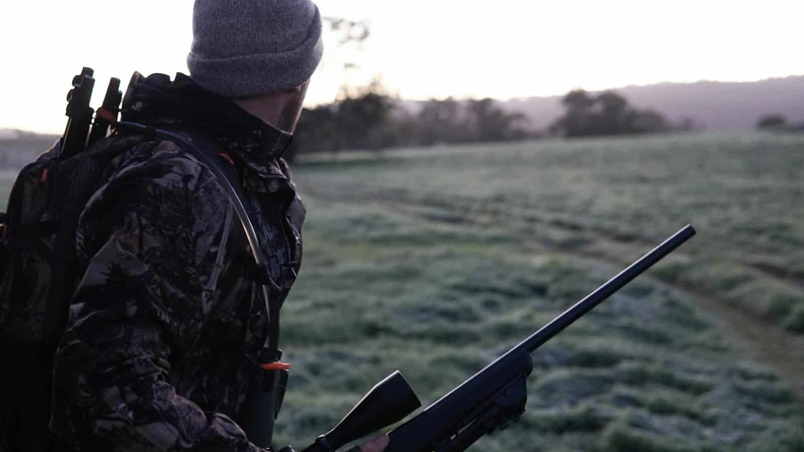 Camouflaged hunter surveying the landscape with rifle at dawn in Victoria, Australia.