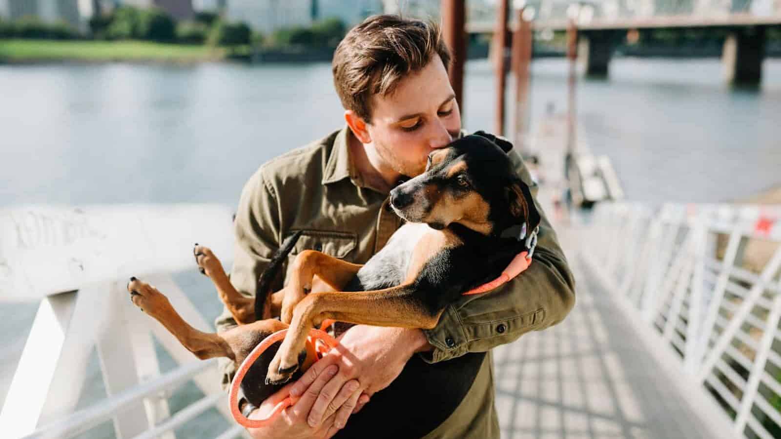 man in brown jacket hugging black and brown short coated dog