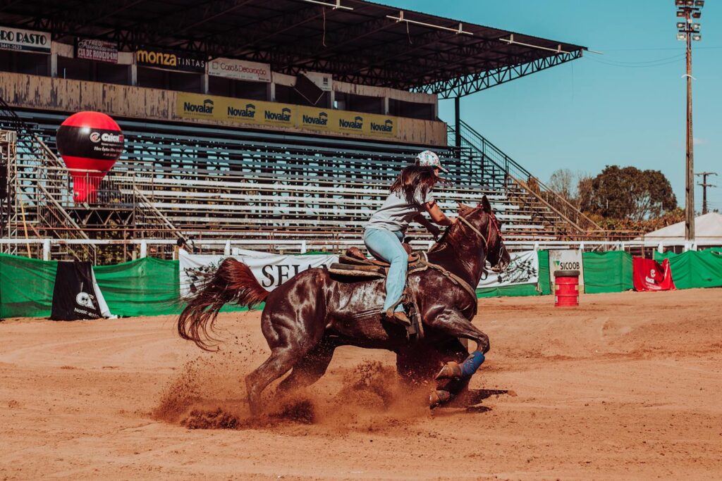 A woman expertly rides a horse at high speed in an outdoor arena, showcasing skill and motion.