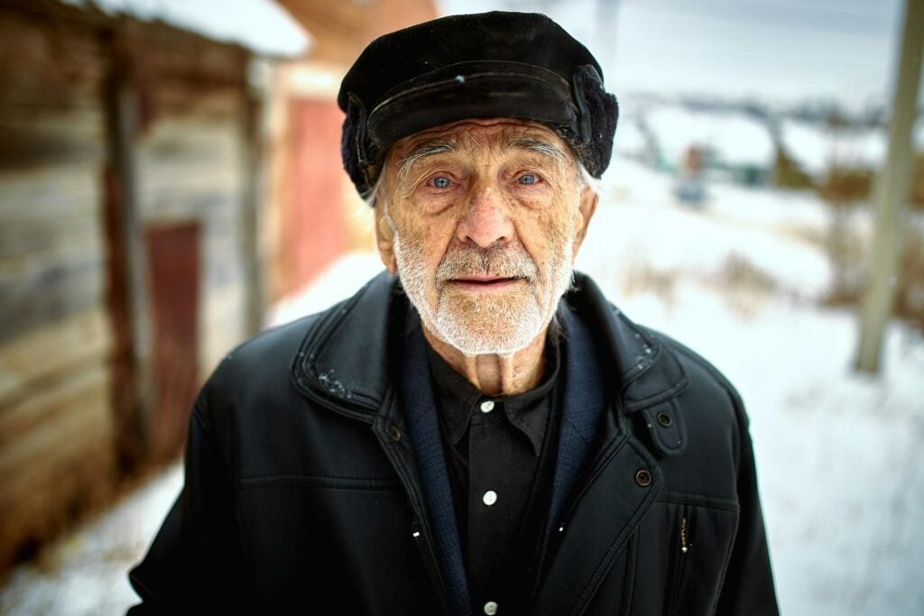 Portrait of an elderly man with a beard wearing warm clothes outdoors in winter.
