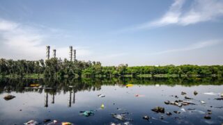View of a polluted river reflecting factory emissions under a clear sky in India.
