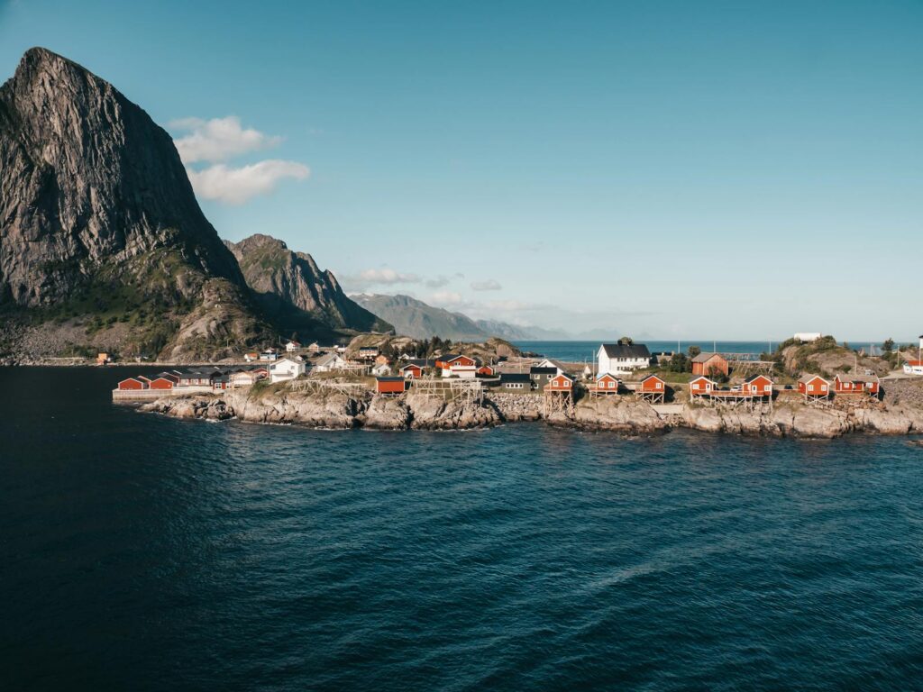 Panoramic view of a coastal village with red houses against a mountain and fjord backdrop in Norway.