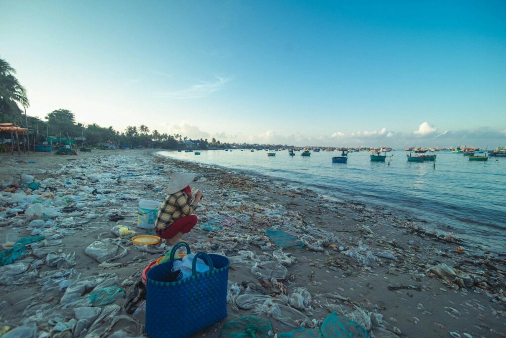A beach covered with plastic pollution, highlighting environmental issues. Fishing boats are visible.
