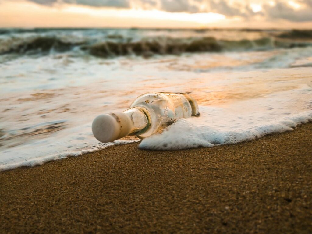 Ground level of empty glass bottle thrown on beach of foaming ocean in evening