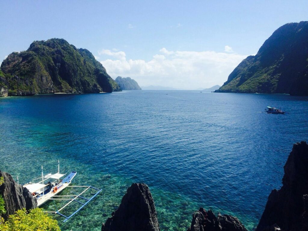 Crystal clear tropical lagoon with boats amidst stunning cliffs and deep blue waters.