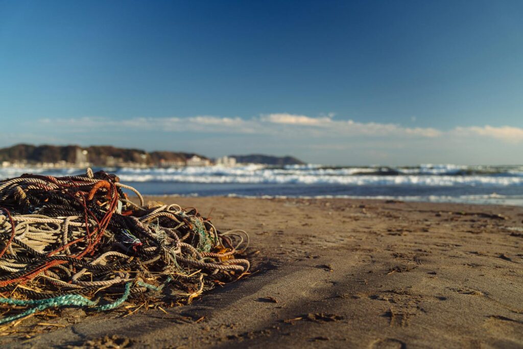 Colorful ropes piled on Kamakura beach, Japan, with ocean waves in the background.