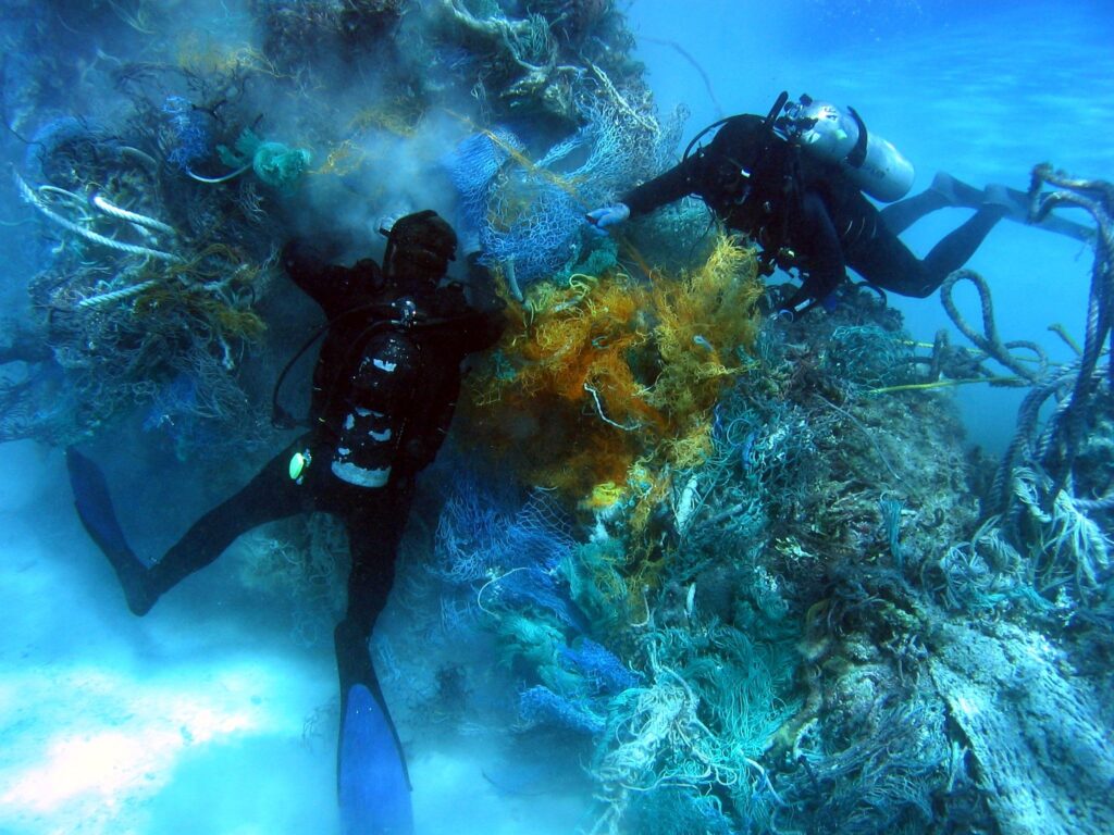 two divers with scuba gear handling waste fishing net from the reef
