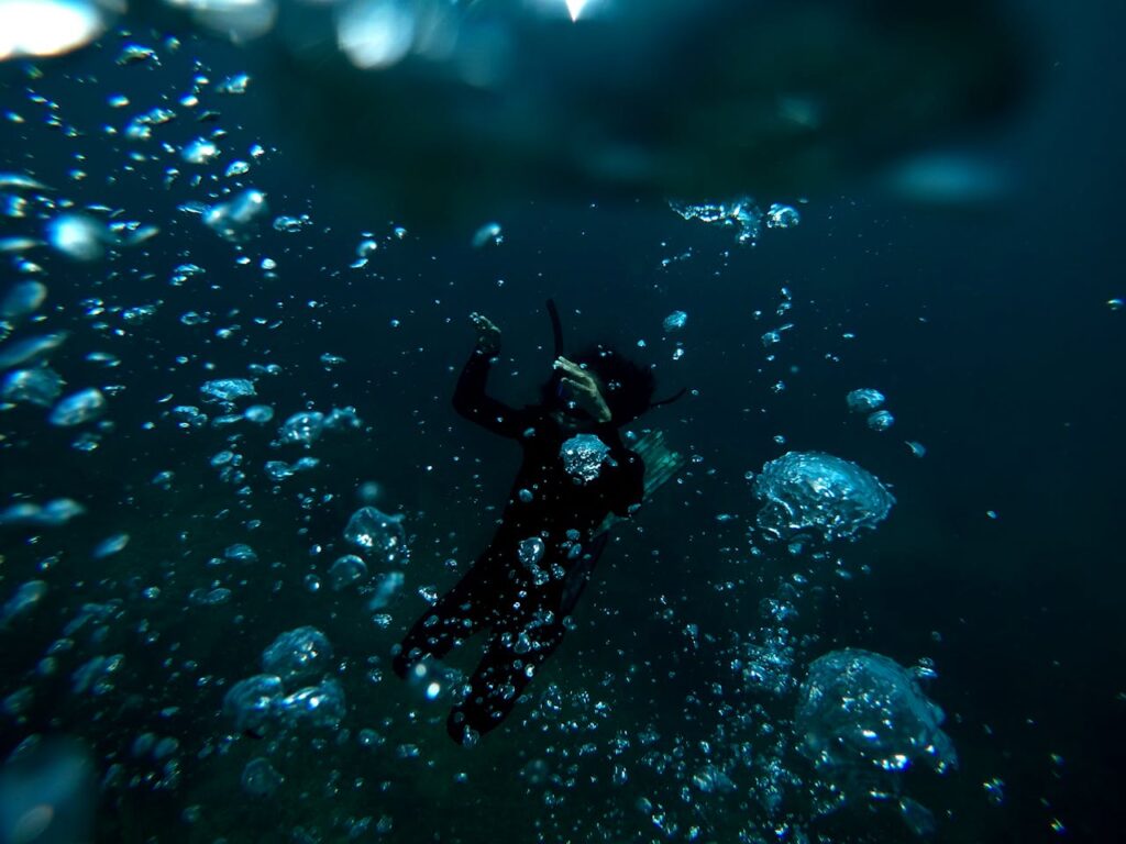 person swimming underwater with surrounding air bubbles